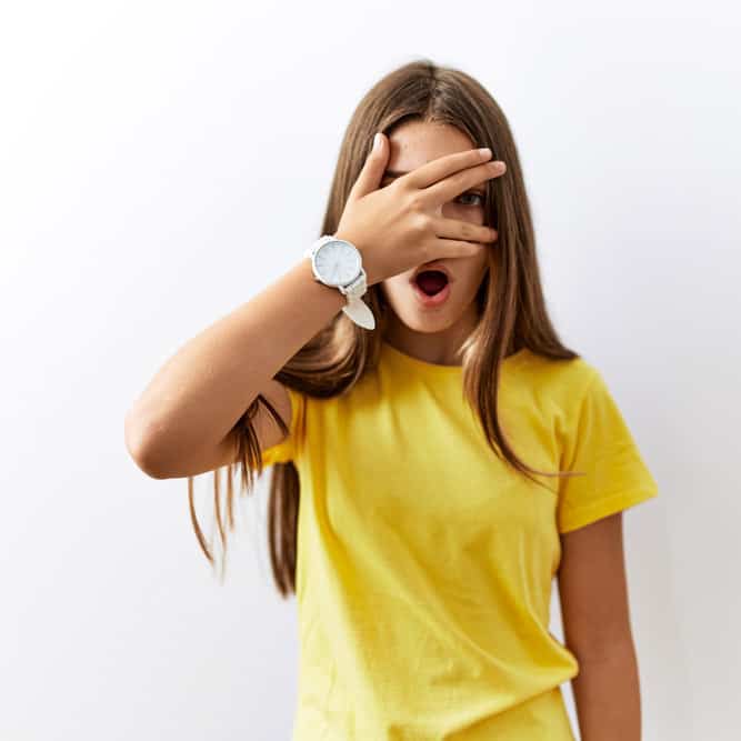 Young brunette teenager standing together over isolated background peeking in shock covering face and eyes with hand, looking through fingers with embarrassed expression.