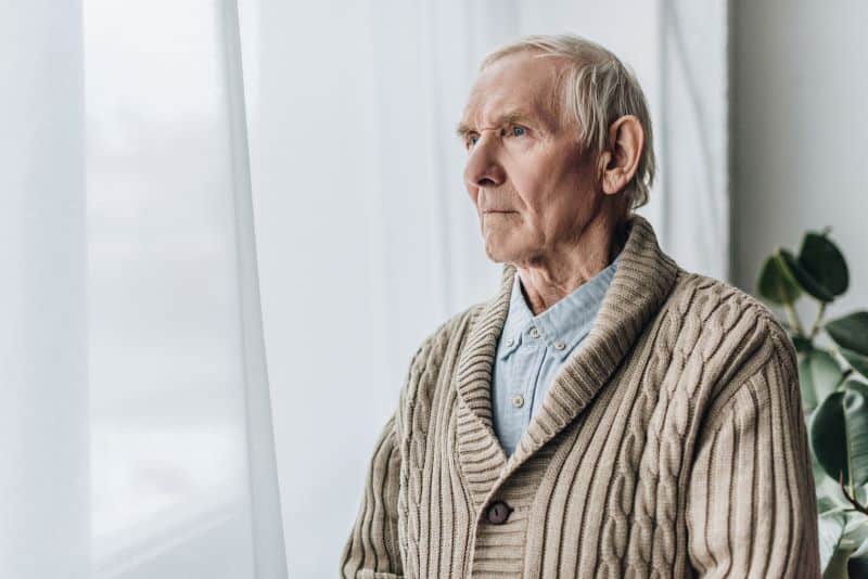 elderly man sitting and looking out a window