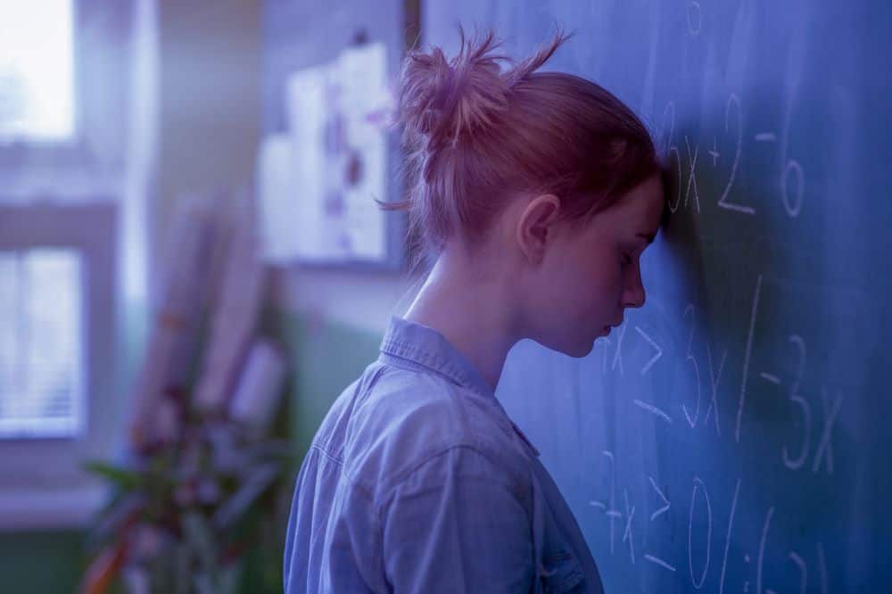 girl with math phobia and anxiety resting head on blackboard