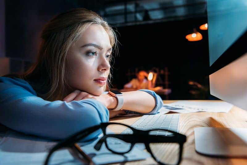 a woman with her hands and head rested on a desk, a computer is next to her